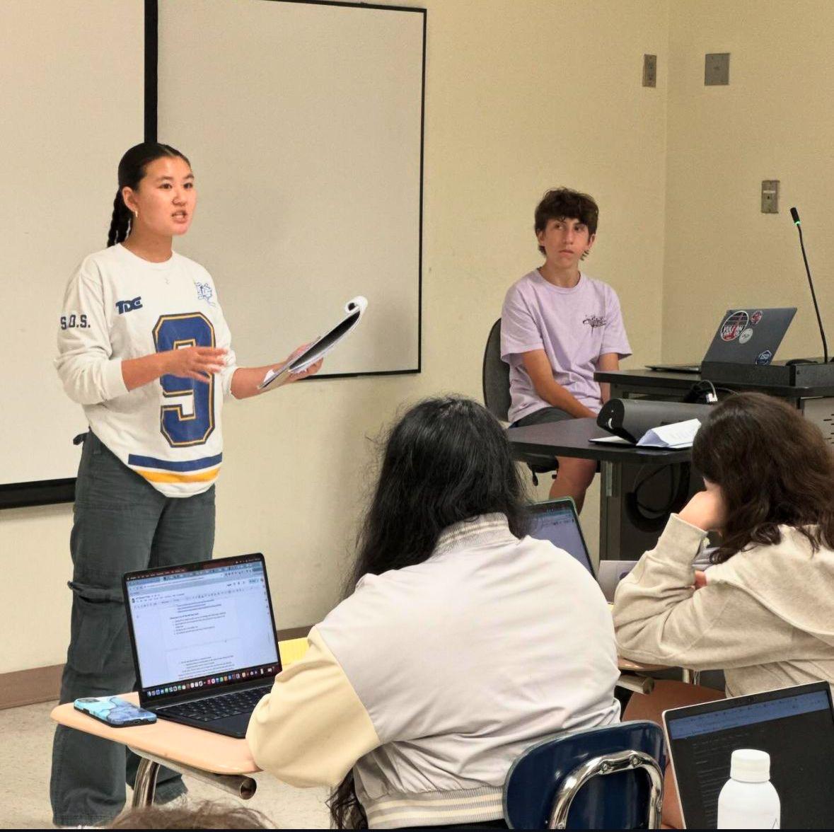 A coach leading a lesson while students review case materials on their laptops